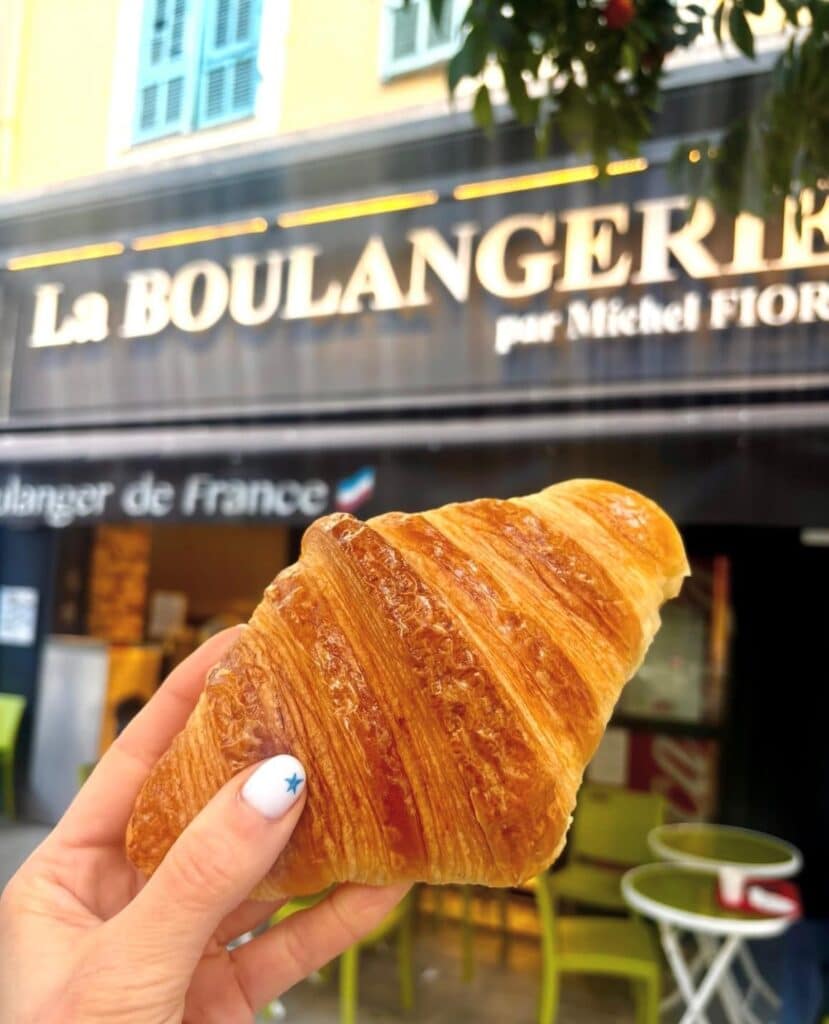 Un croissant tenu dans une main devant la devanture noir de la boulangerie Michel Fiori