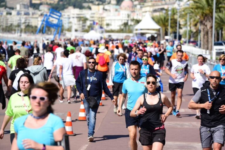 Des centaines de personnes en train de courir en tenue de sport ou marcher en tenue de ville sur la Promenade des Anglais en face de la mer.