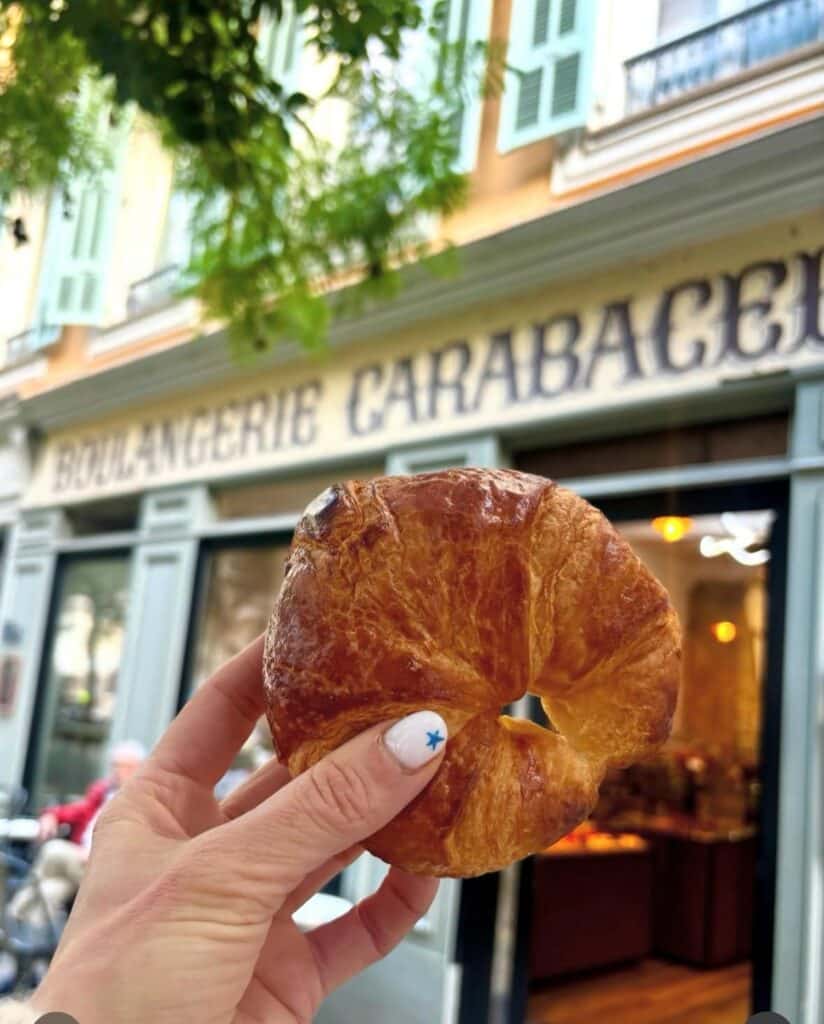 Un croissant tenu dans une main devant la devanture de pains et carabacel.