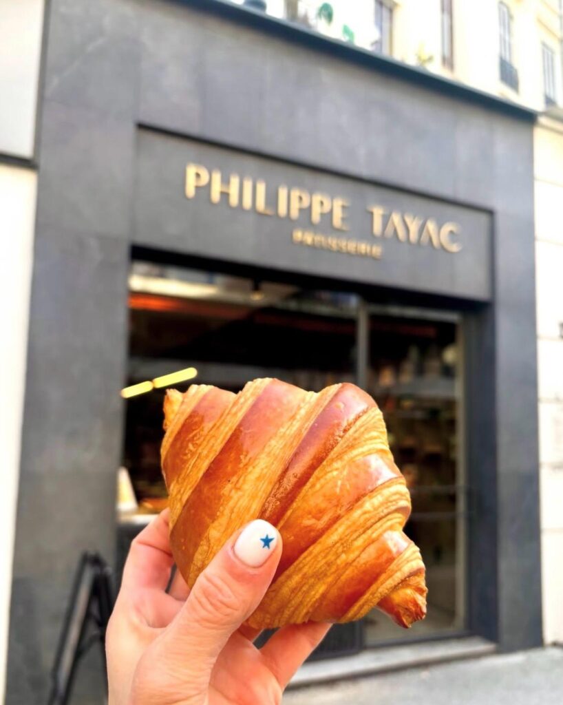 Un croissant tenu dans une main devant la devanture noir de chez Philippe Tayac.