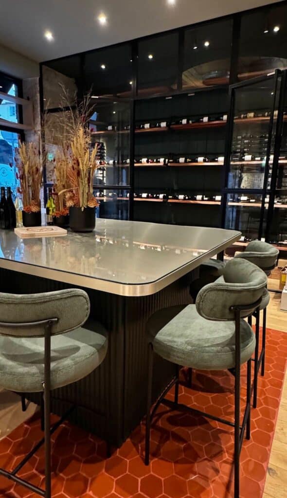 Une table de dégustation style zinc de bar avec des chiasses hautes en velour vert.