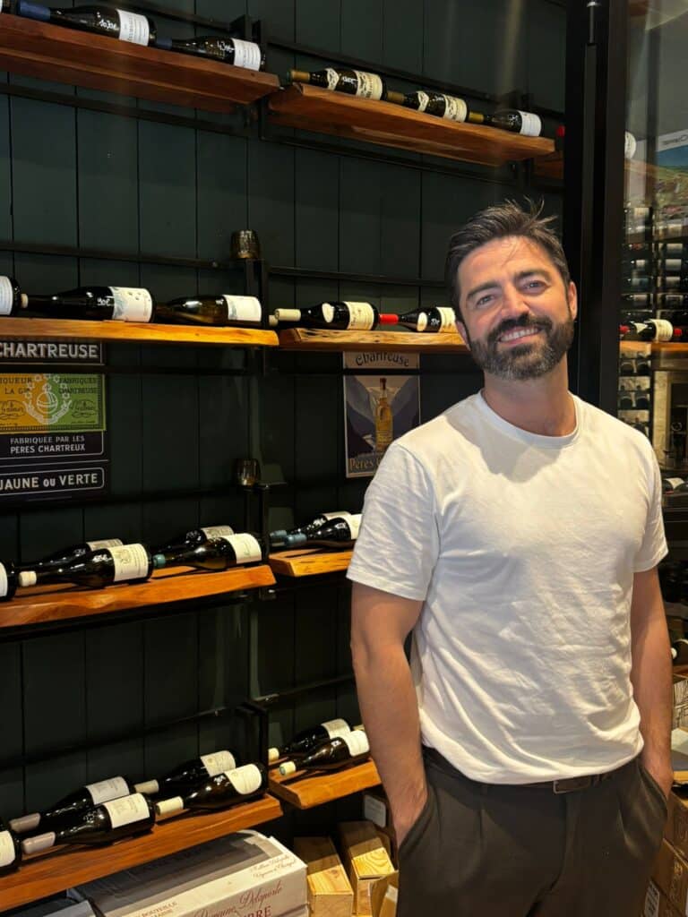 Dorian, le co-gérant de Pinot et Chardo, pose fièrement devant une partie de sa cave