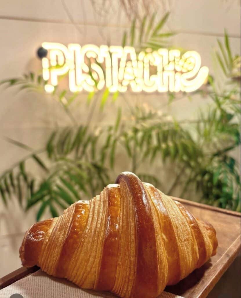 Un croissant tenu dans une main dans la boutique de Pistache, avec le nom de l'enseigne éclairée avec des LED.