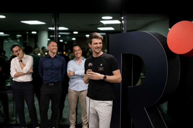 Trois des quatre associés de Recordia devant leur logo en grand. L'un d'entre eux tient un micro pour s'exprimer devant les invités.