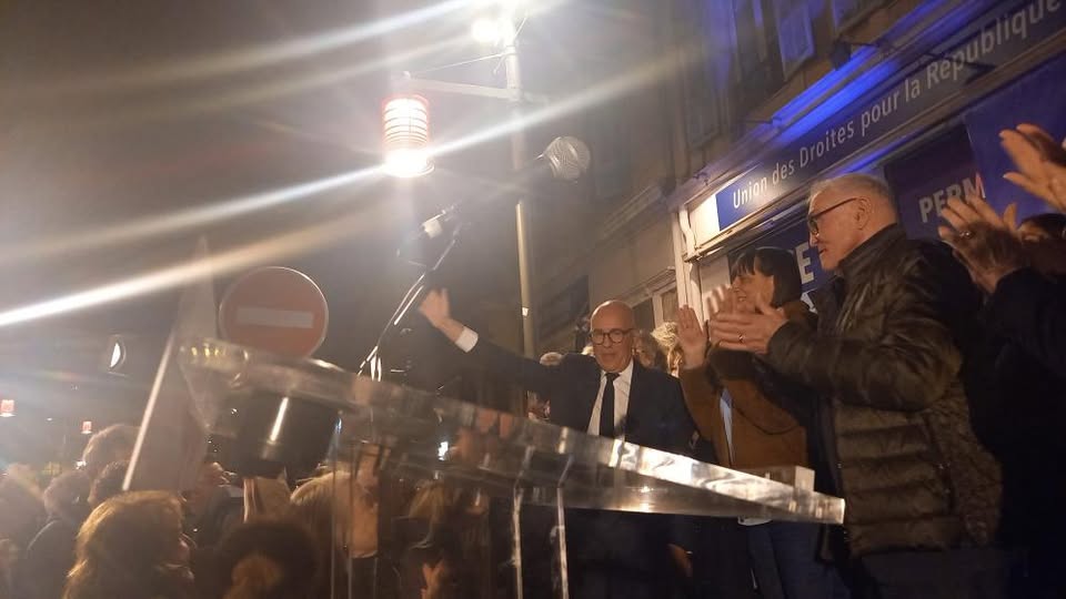 arrivée du candidat eric ciotti sur l'estrade devant sa permanence qui leve le bras marchant vers son pupitre