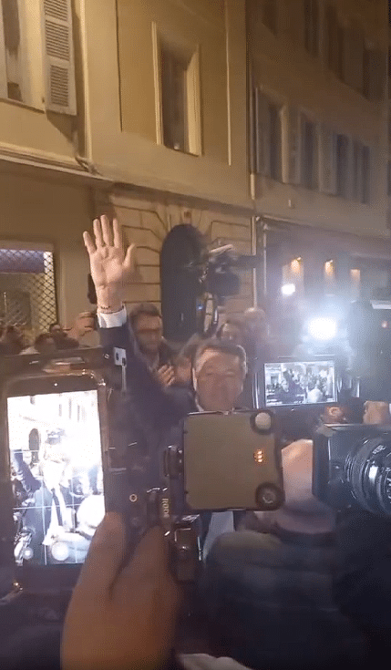 Christian Estrosi maire sortant dit aurevoir à la foule la main droite en l'air éblouit par les flashs des appareils photos à la sortie de sa permanence