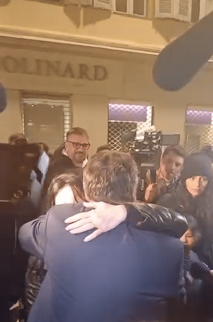 Christian Estrosi maire sortant dit aurevoir à la foule en enlaçant une femme éblouit par les flashs des appareils photos à la sortie de sa permanence