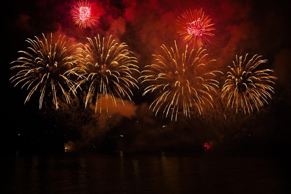 Le feu d'artifice du Carnaval de Nice tiré sur la mer devant la Promenade des Anglais. Une explosion de couleurs rouge, oragne et jaune.