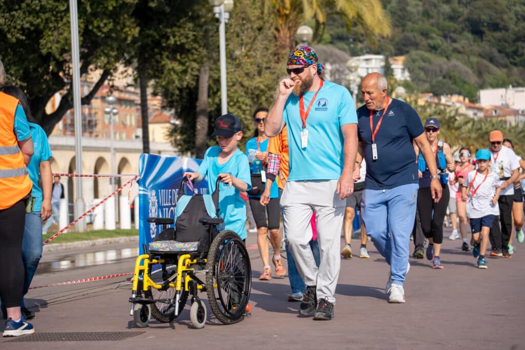Un jeune accompagné pousse son fauteuil roulant durant la No Finish Line 2026 à Nice.