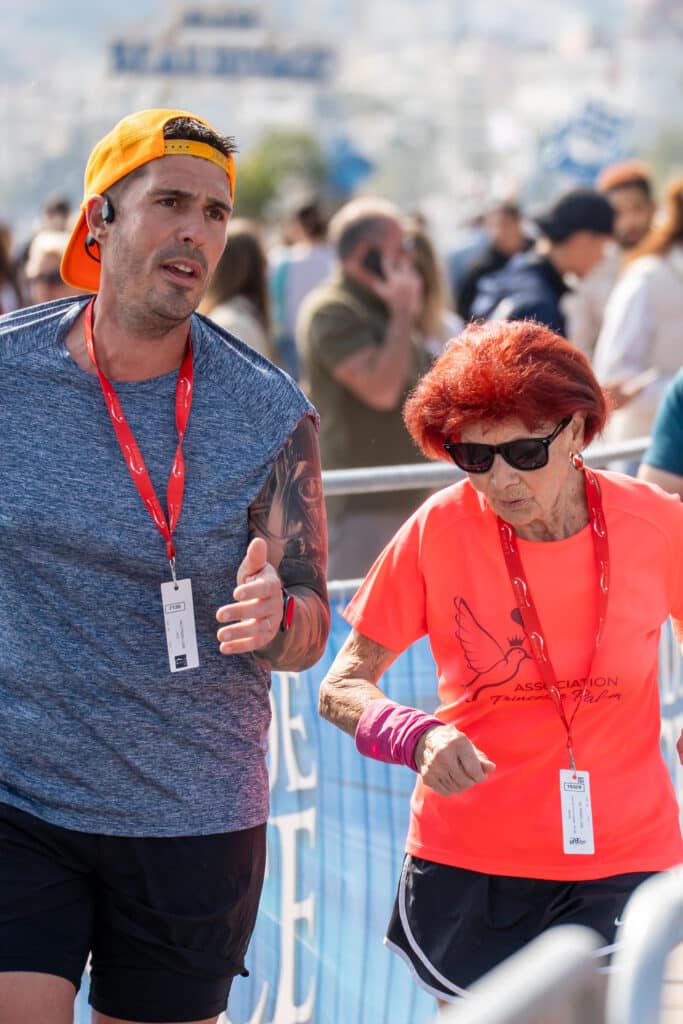 Une personne agée en tee-shirt orange court à côté d'un autre participant lors de la No Finish Line 2026 de Nice.