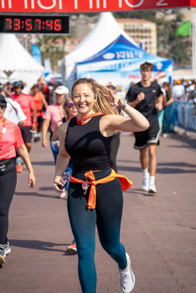 Une participante de la No Finish Line 2026 de Nice court en faisant un signe au photographe avec le sourire.