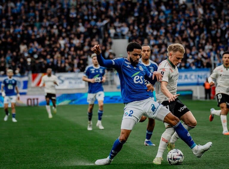 Un joueur de l'OGC Nice en blanc se fait déposséder du ballon par un joueur de Strasboug en bleu.