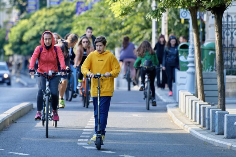 Un enfant en trottinette électrique sans équipement de protection au milieu des vélos sur une voie de circulation.
