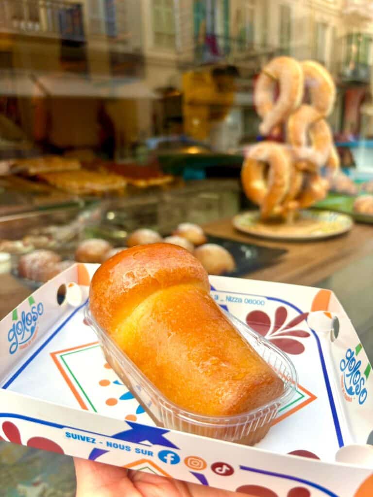 Le Baba au rhum du coffee shop Napolitain dans une barquette en plaqtique posée dans une assiette. Il a une forme longue.