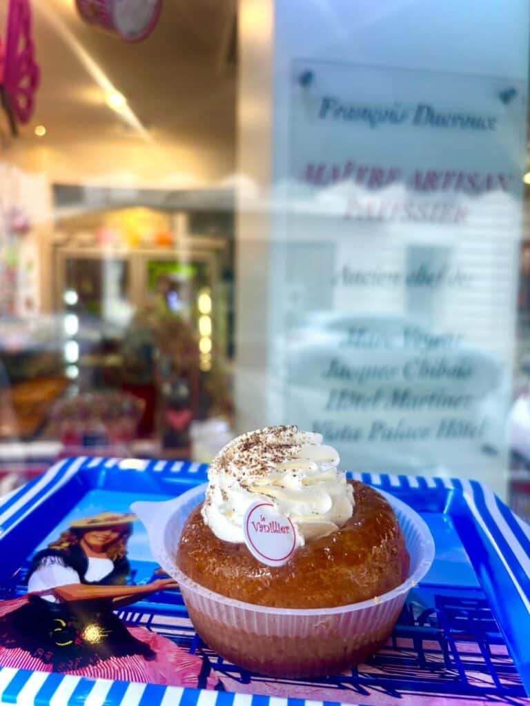 Le baba au rhum de la pâtisserie Le Vanillier dans un barquette en plastique avec de la cr^me sur le dessus.