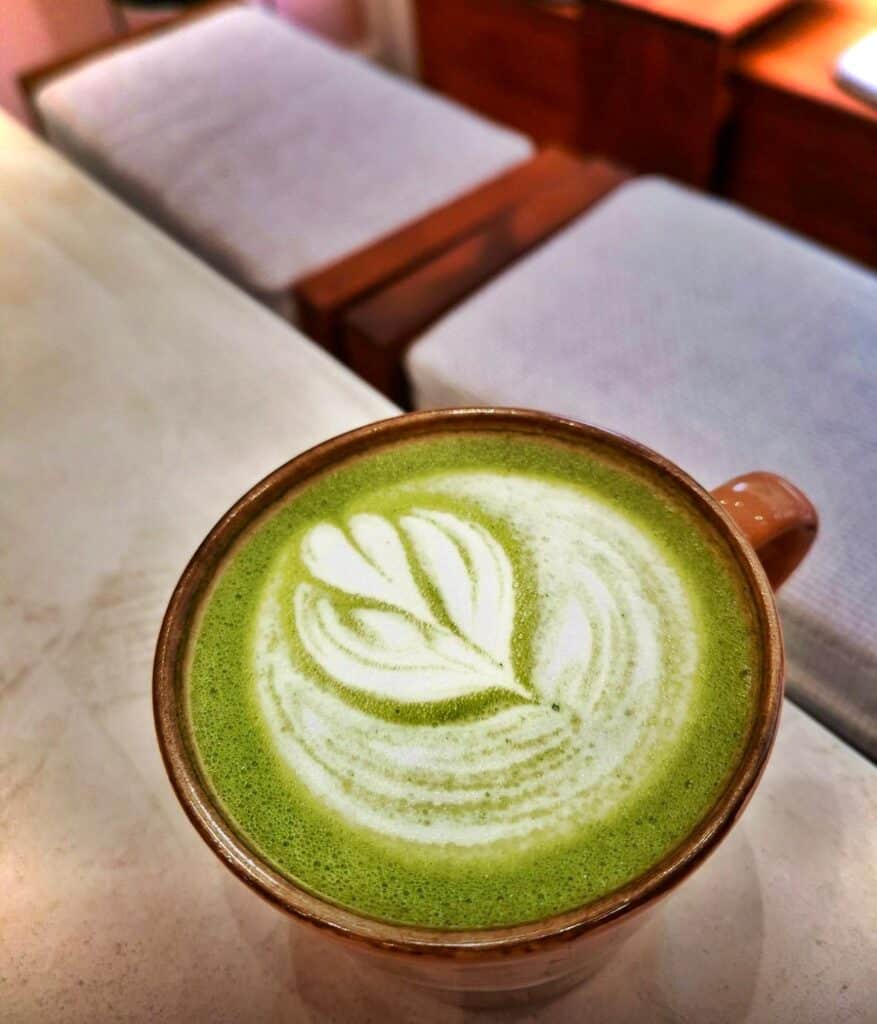 Une boisson verte dans une tasse avec un dessin fait avec du lait sur le dessus.