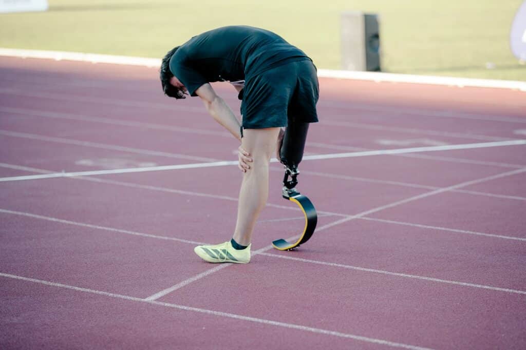 Un athlète handisport avec une prothèse de hanche à l'arrivée de sa course les mains sur le genou et sa prothèse.
