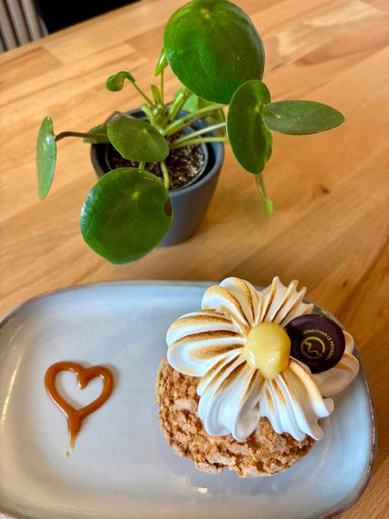 Un choux au citron avec une crème chantilly dessus et un coeur en fruit rouge à côté dans une assiette.