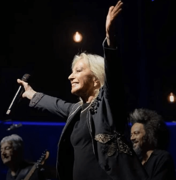 L'artiste Véronique Sanson en noir les bras ouvert comme pour saluer la foule avec un grand sourire.