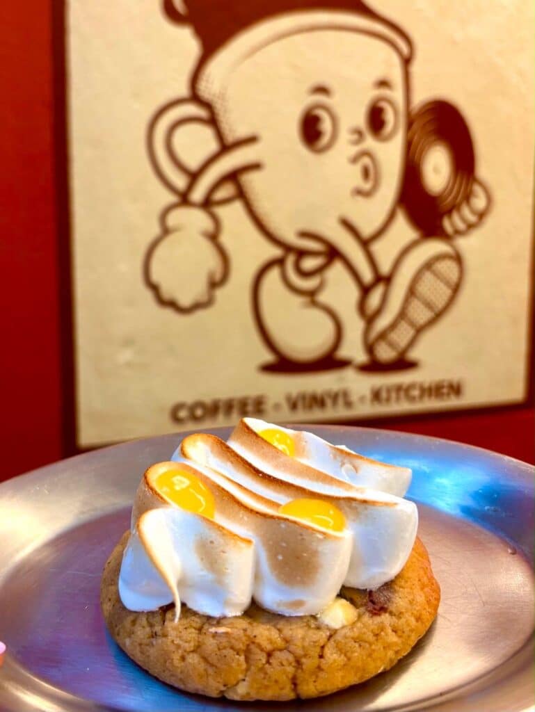 Un cookie au citron avec de la meringue fondue sur le dessus et une affiche représentant une tasse à café en forme humaine en arrière plan.