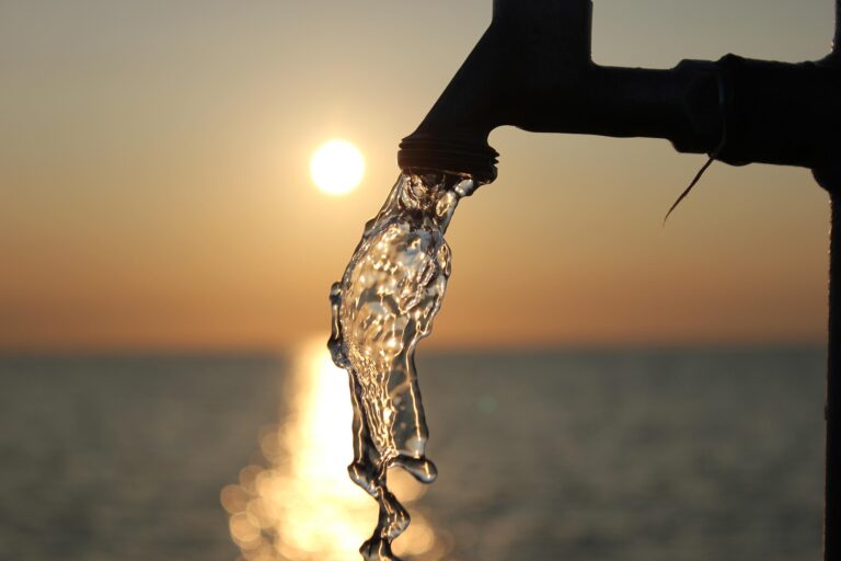 un robinet d'eau qui coule devant le soleil et une grande marre d'eau.