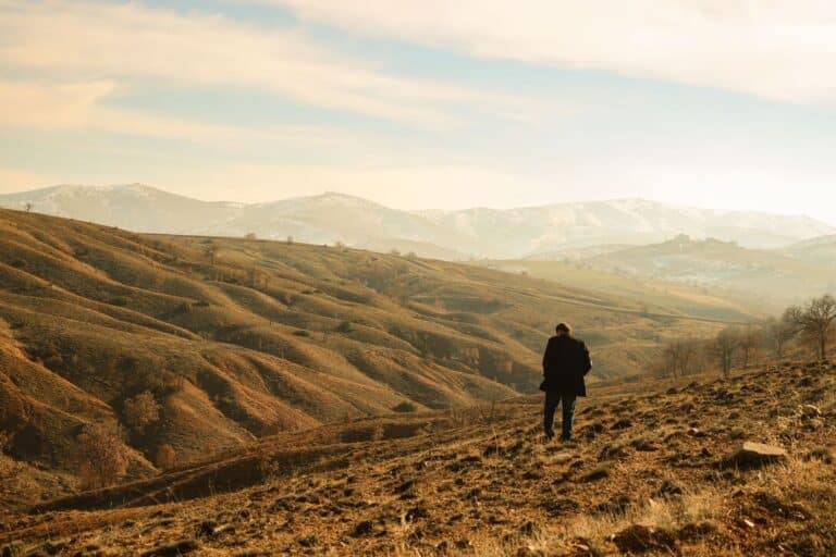 Une personne seule se tenant au milieu des collines et des montagnes sous un ciel dégagé.