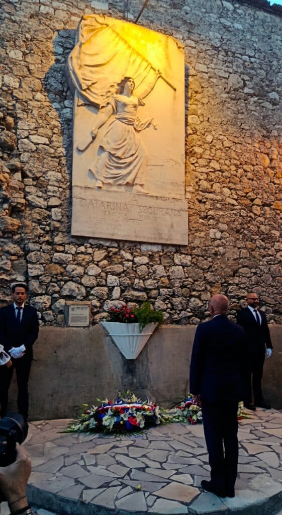 Eric Ciotti devant la stèle hommage à Catherine Ségurane avec un bouquet de fleur posée devant.