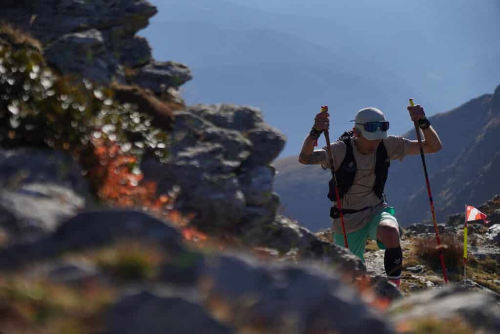 Un coureur avec ses bâtons en pleine montée dans la montagne.