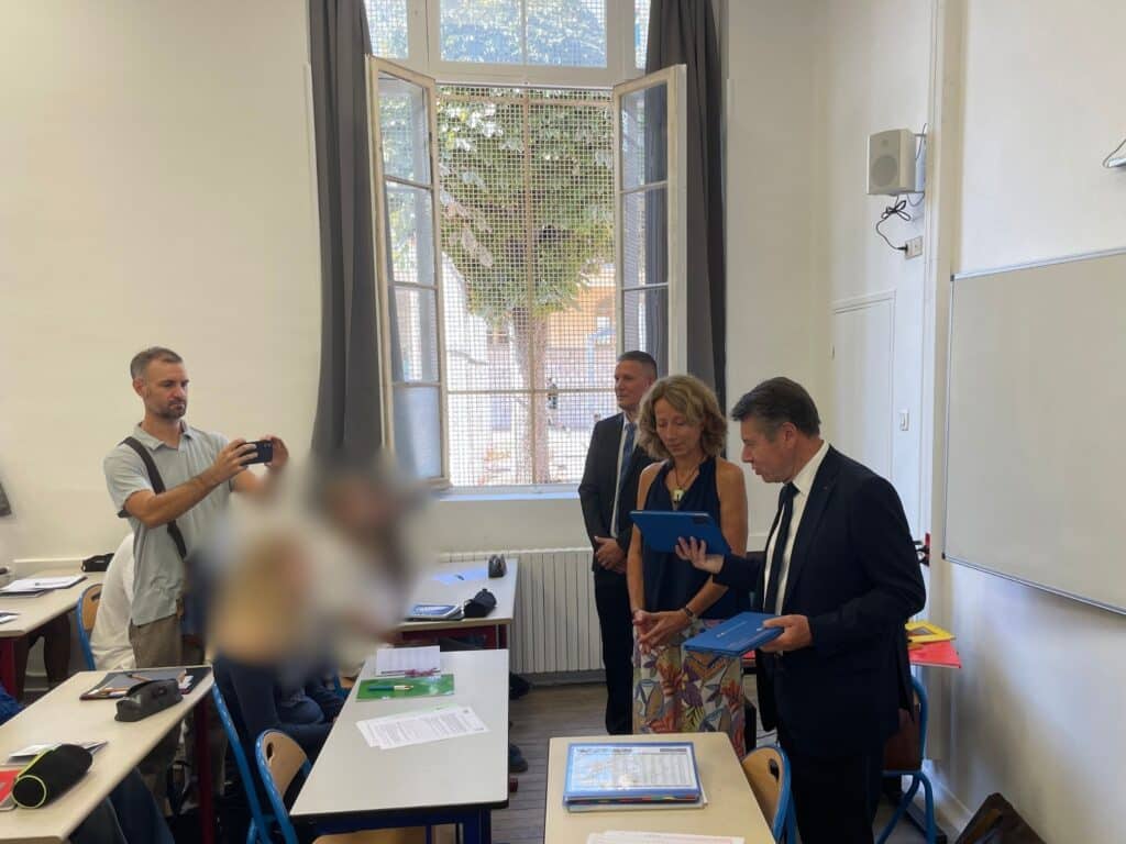 Christian Estrosi debout en costume dans une salle de classe avec des tablettes tactiles en main