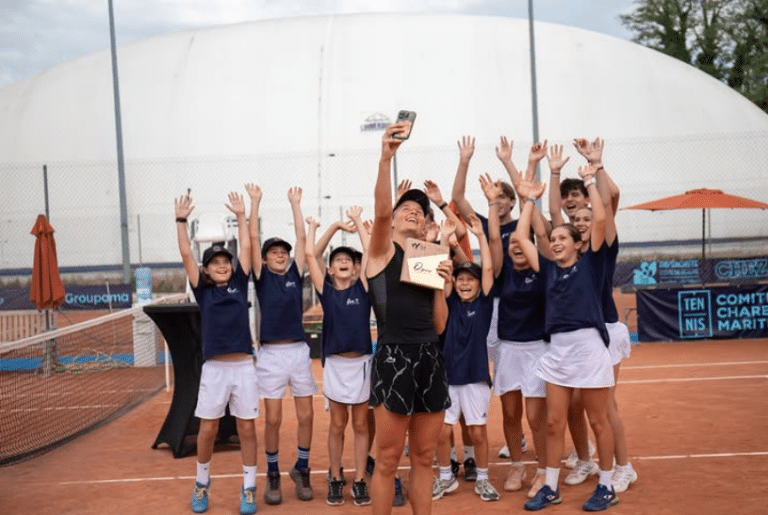 La Valbonnaise Fiona Ferro pose avec les ramasseurs de balles et son trophée dans les mains sur un court en terre battue.