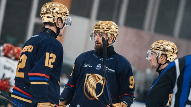 Des joueurs des Aigles de Nice en Ligue Magnus se parlent en tenue bleu avec l'aigle sur le torse couleur dorée.