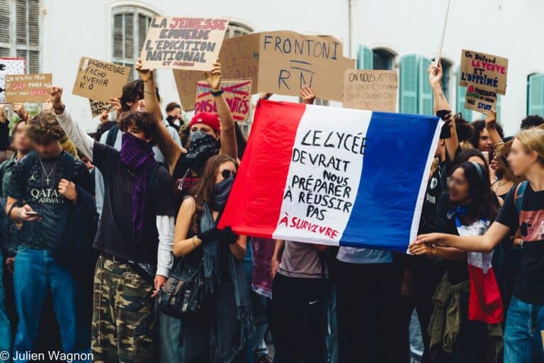 Des étudiants avec un drapeau français annoté de l'inscription : "Le lycée devrait nous préparer à réussir pas à survivre."